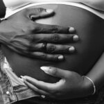 Black and white image of a woman and hr partner's hand on her pregnant belly via Freepik