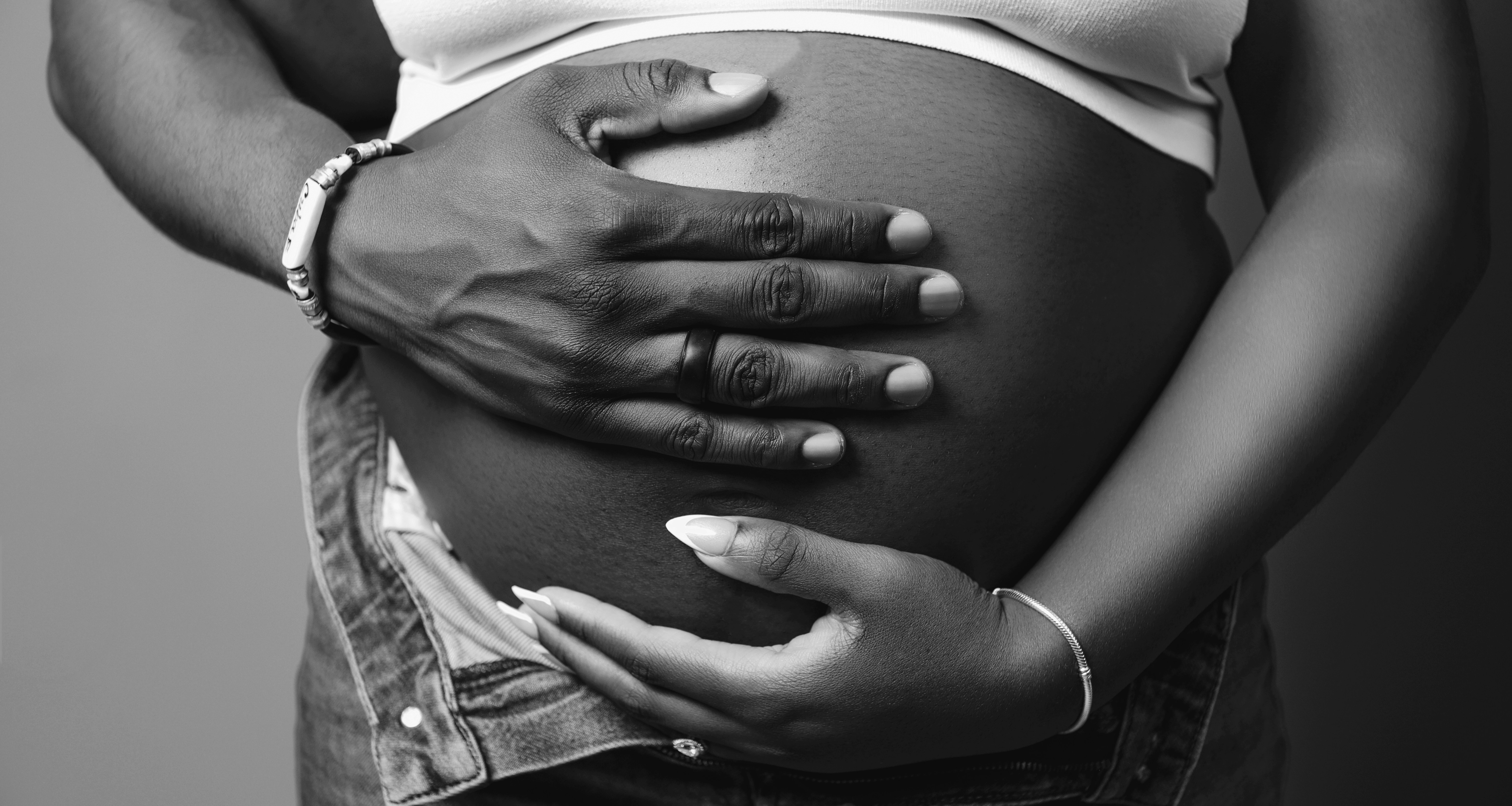 Black and white image of a woman and hr partner's hand on her pregnant belly via Freepik
