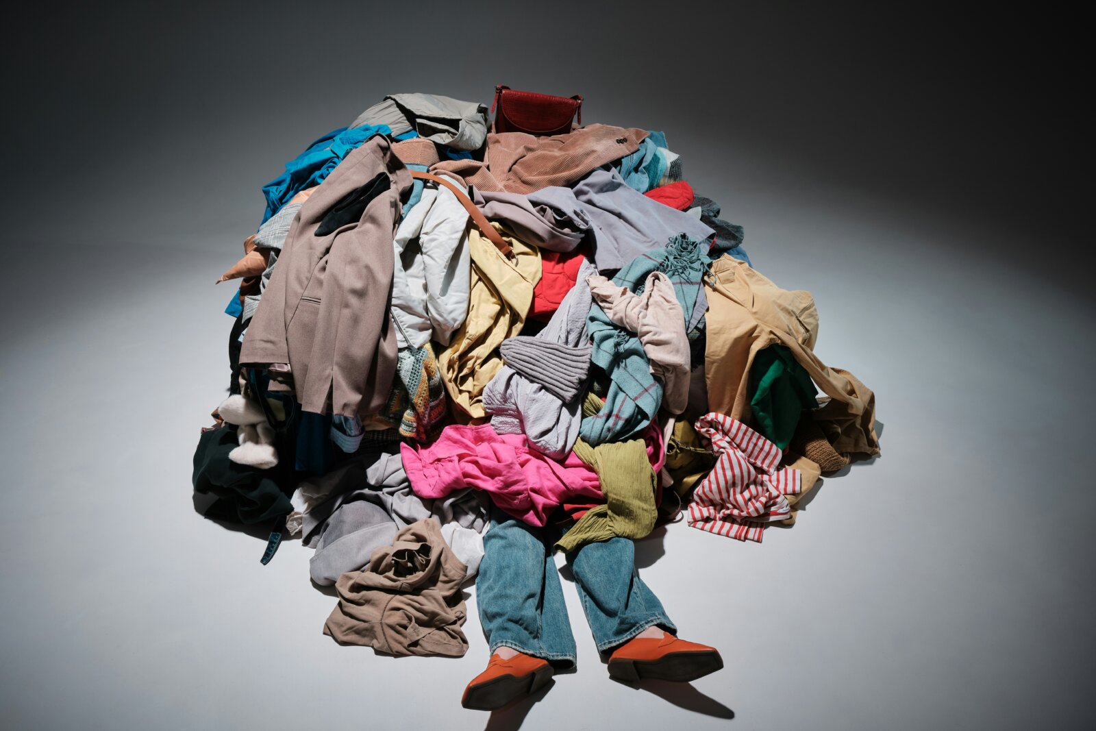 Shein; Image of a person under a heap of clothes by Andrej Lišakov via Unsplash+