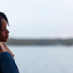A sad, contemplative black woman staring out at a body of water via Freepik