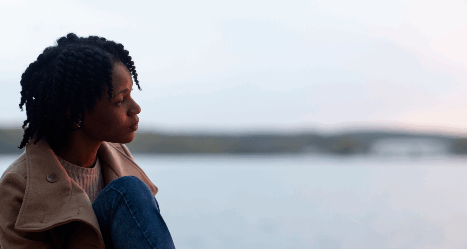 A sad, contemplative black woman staring out at a body of water via Freepik