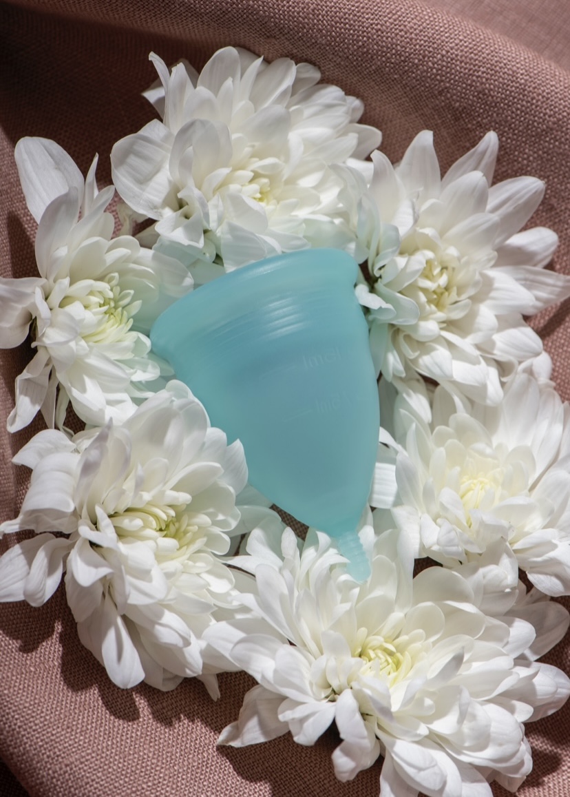 A blue menstrual cup surrounded with white flowers via Freepik