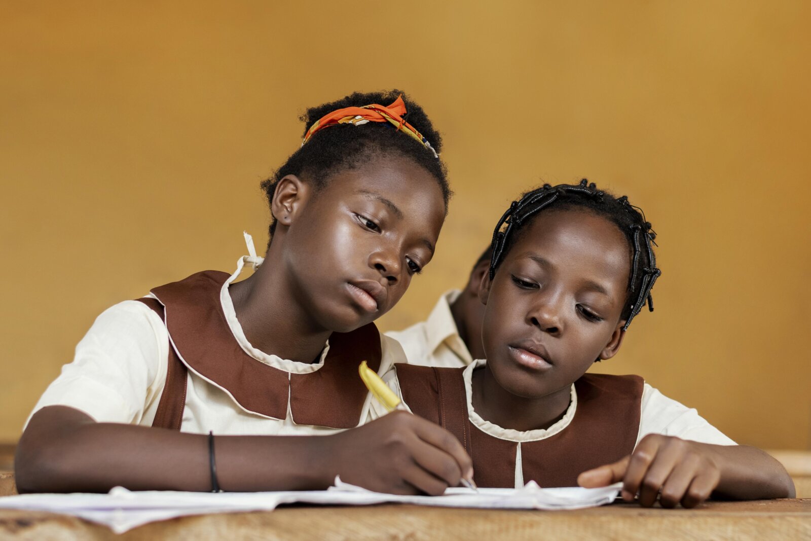 Two girls in uniform writing in a book via Freepik