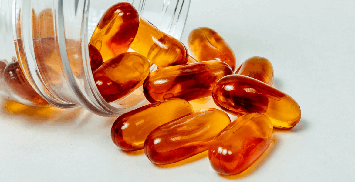 A transparent medicine bottle with amber capsules spewing from it