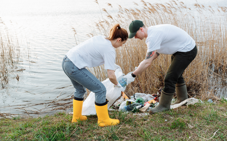 Man and woman cleaning up litter near a river