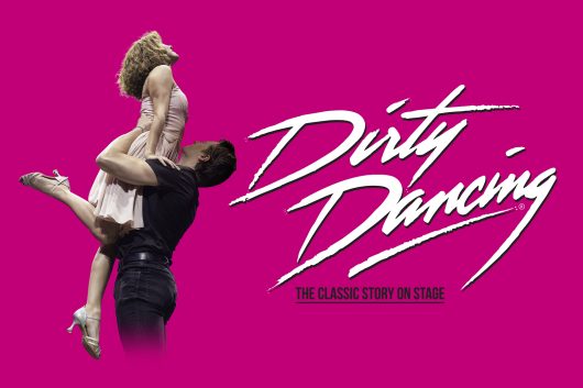 A promotional image for “Dirty Dancing: The Classic Story on Stage” featuring a man in a black shirt lifting a woman in a pale pink dress in an iconic dance pose against a bright pink background, with the white “Dirty Dancing” logo displayed prominently on the right.