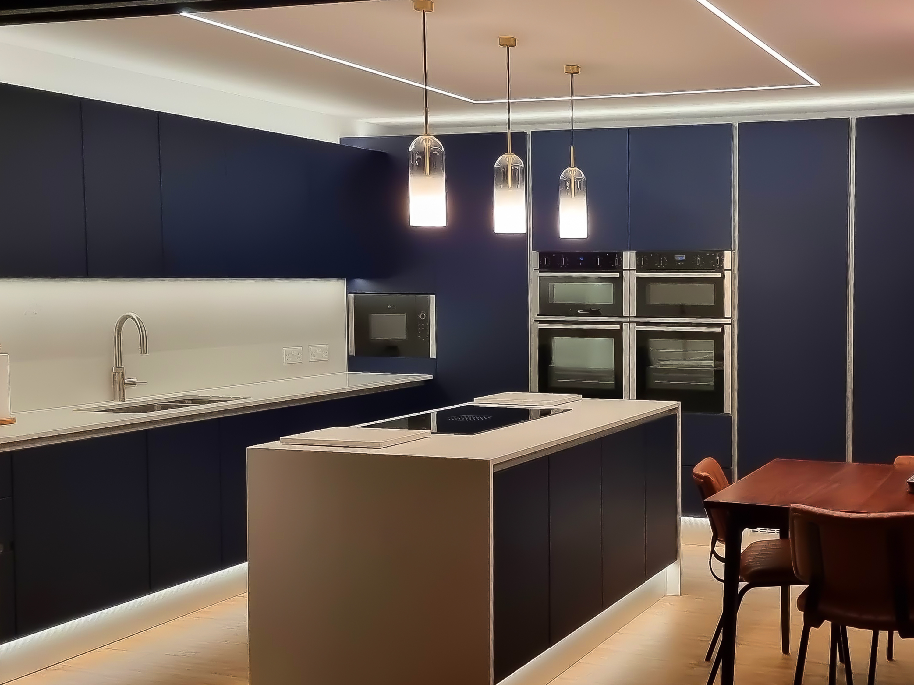 Modern navy kitchen with LED profile ceiling lines, glass pendants over the island and plinth lighting