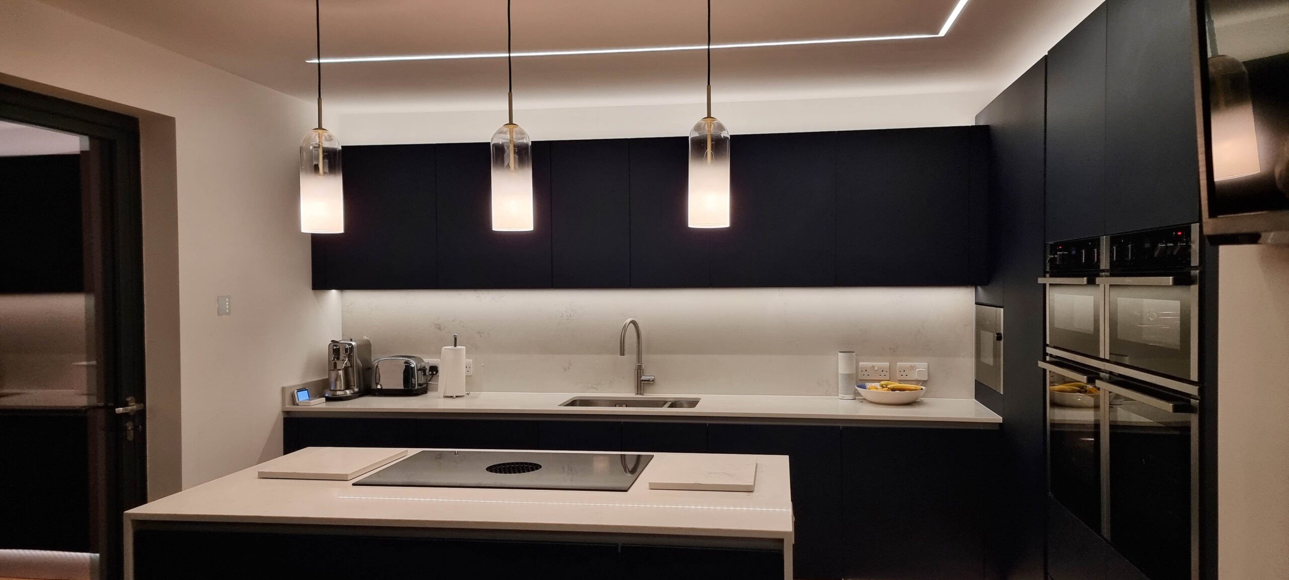 Modern kitchen with three glass pendant lights, LED strip in a ceiling recess and under cabinet lighting over a worktop