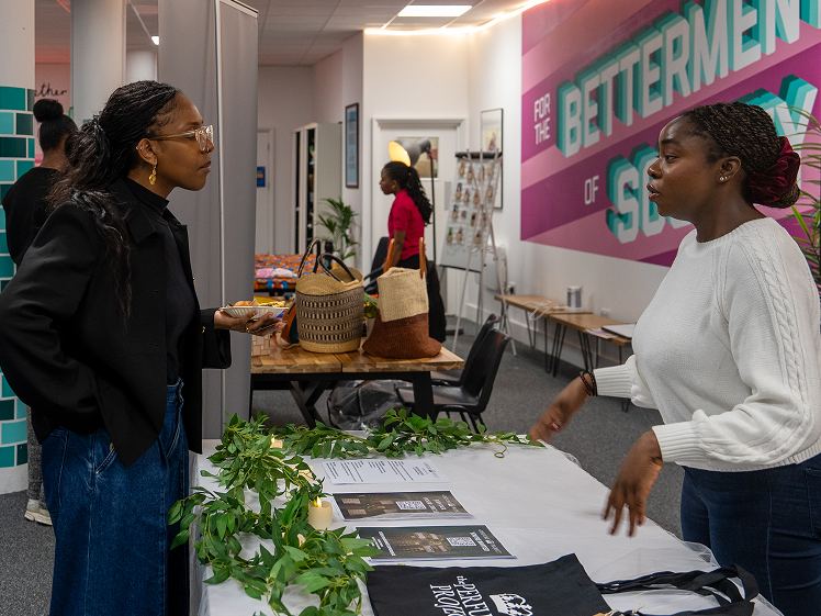 Two woman in discussion at a stall talking about supporting inclusivity and innovation.