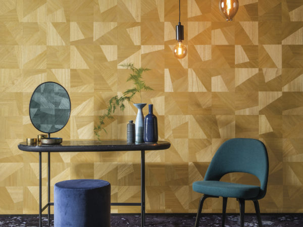 In this picture an example of how the Omexco Sycamore collection embodies natural beauty and soft glamour. A beautiful contrast between the yellow dimensions design of chic interlocking wood textures with green interior details: a chair, pouf, pendulum lights and in the mirror we see the same wallcovering in green appear.