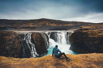 man sitting in front of waterfall