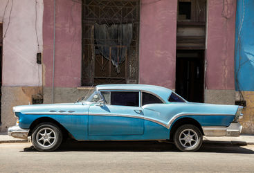 A blue classic car against a pink wall