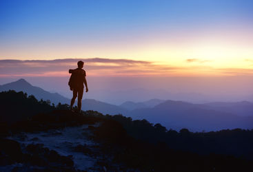 Man stands along on a mountain top at sunset