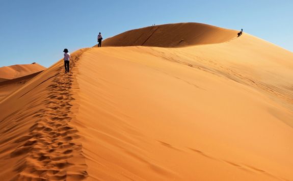 people climbing red sand dunes