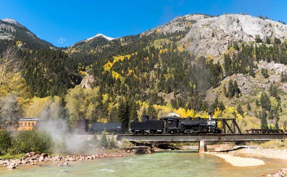 Steam locomotive crossing river and mountain background