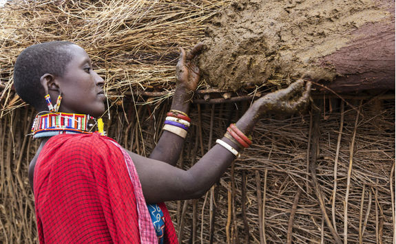 Maasai woman buiding hut putting cows dung on roof