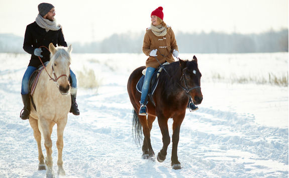 couple horseback riding along snowy trail