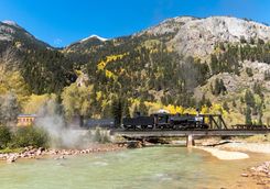 Steam locomotive crossing river and mountain background