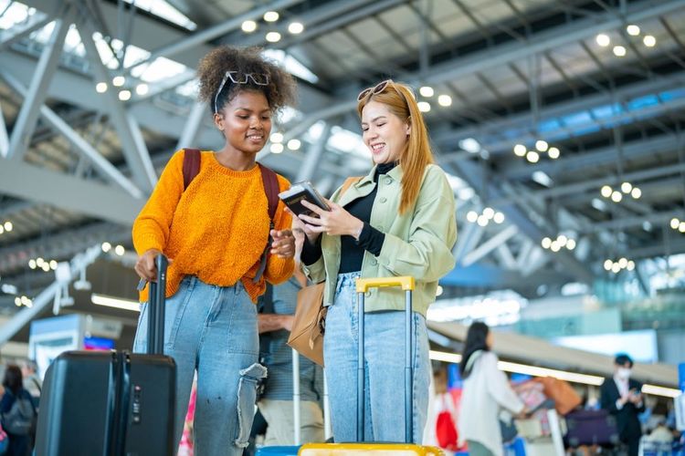 Deux voyageuses consultant une application de budget voyage sur un smartphone dans un aéroport.
