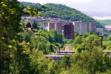 T-bane krysser bro nær Bryn omgitt av trær  bylandskap i avstanden.