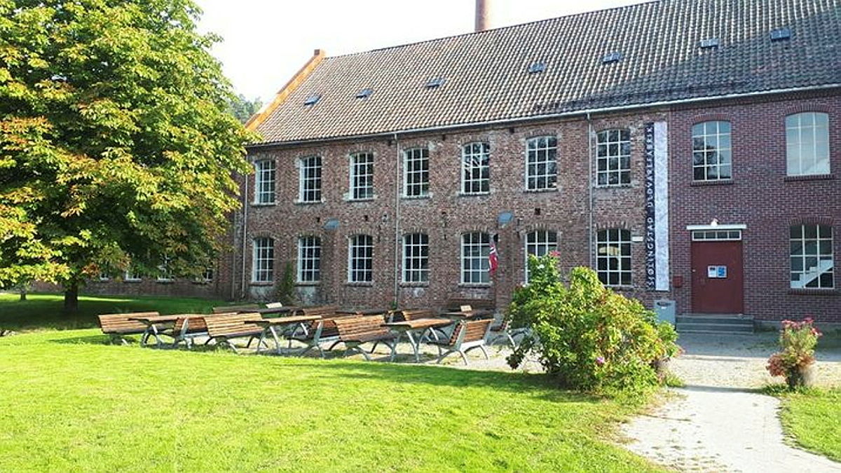 Langstrakt fabrikkbygning i tegl, med to etasjer pluss fullt loft. Nyanser i fasaden viser ulike byggetrinn. Det er to rader med store, sammensatte vinduer i tillegg til en rekke takvindu.