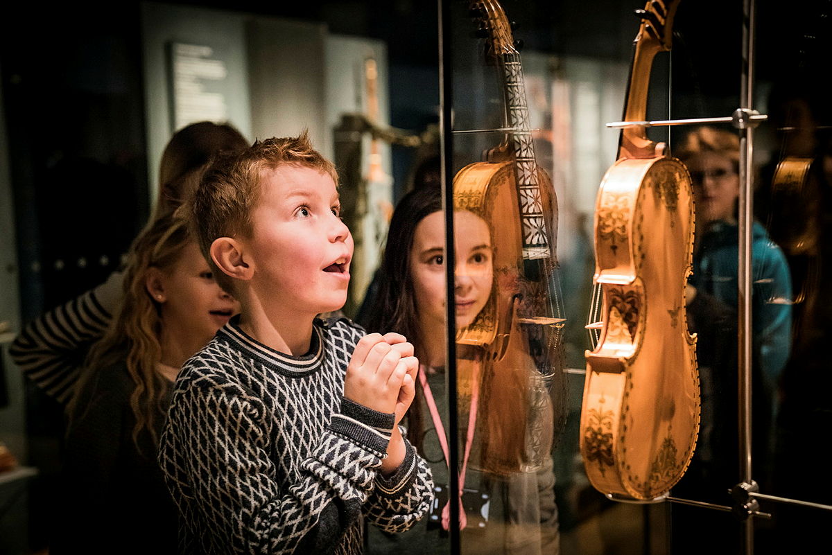 Barn ser i ærefrykt på utsmykkede strengeinstrumenter som vises bak glass i en museumsutstilling.