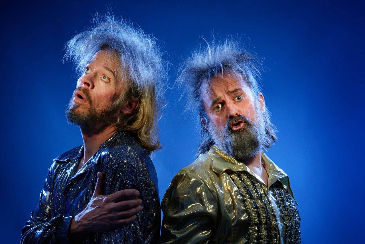 To menn med ruskete hår ser inn i kamera. Grimaser i ansiktet.