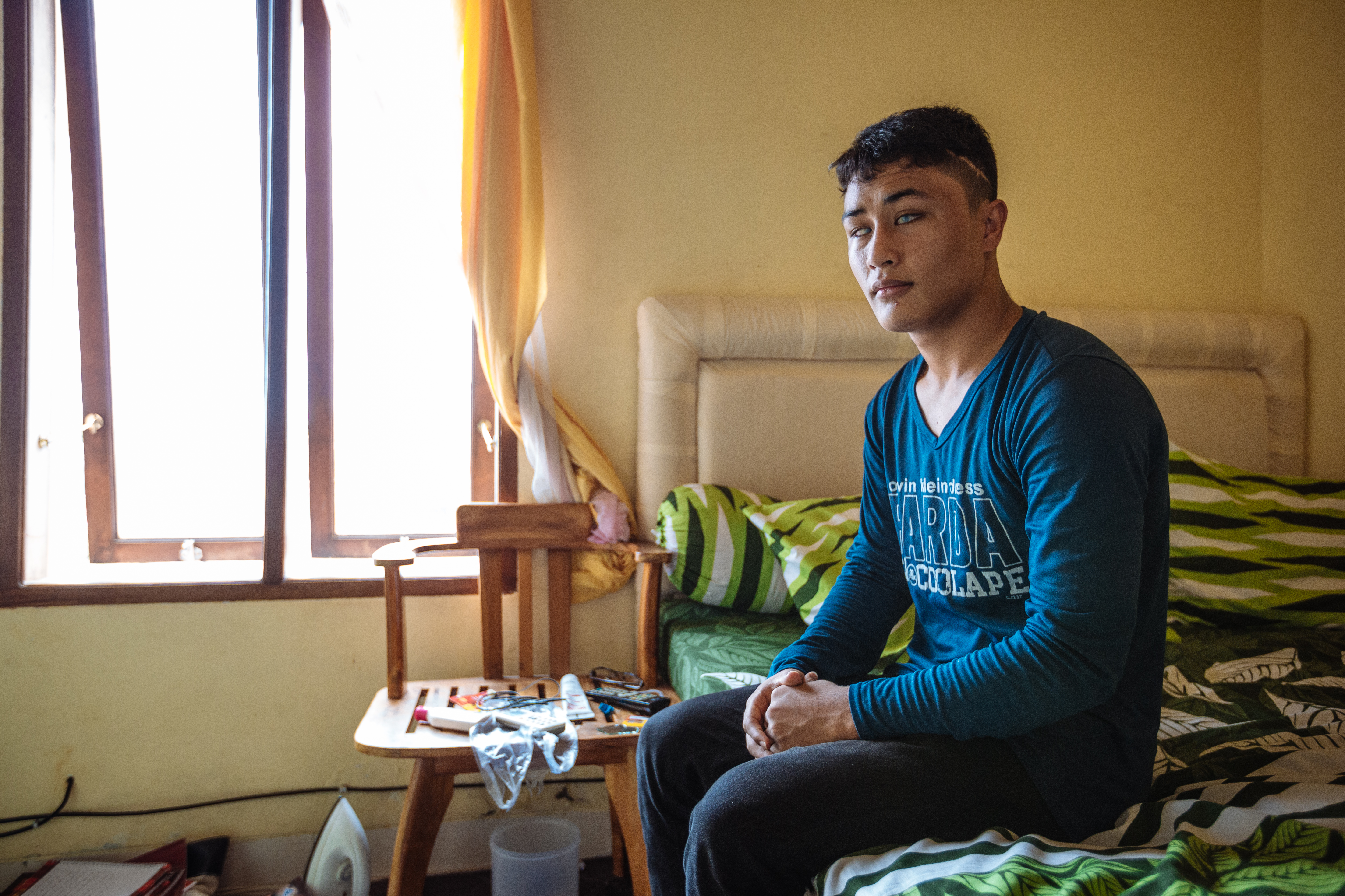 A young blind boy sits on a bed