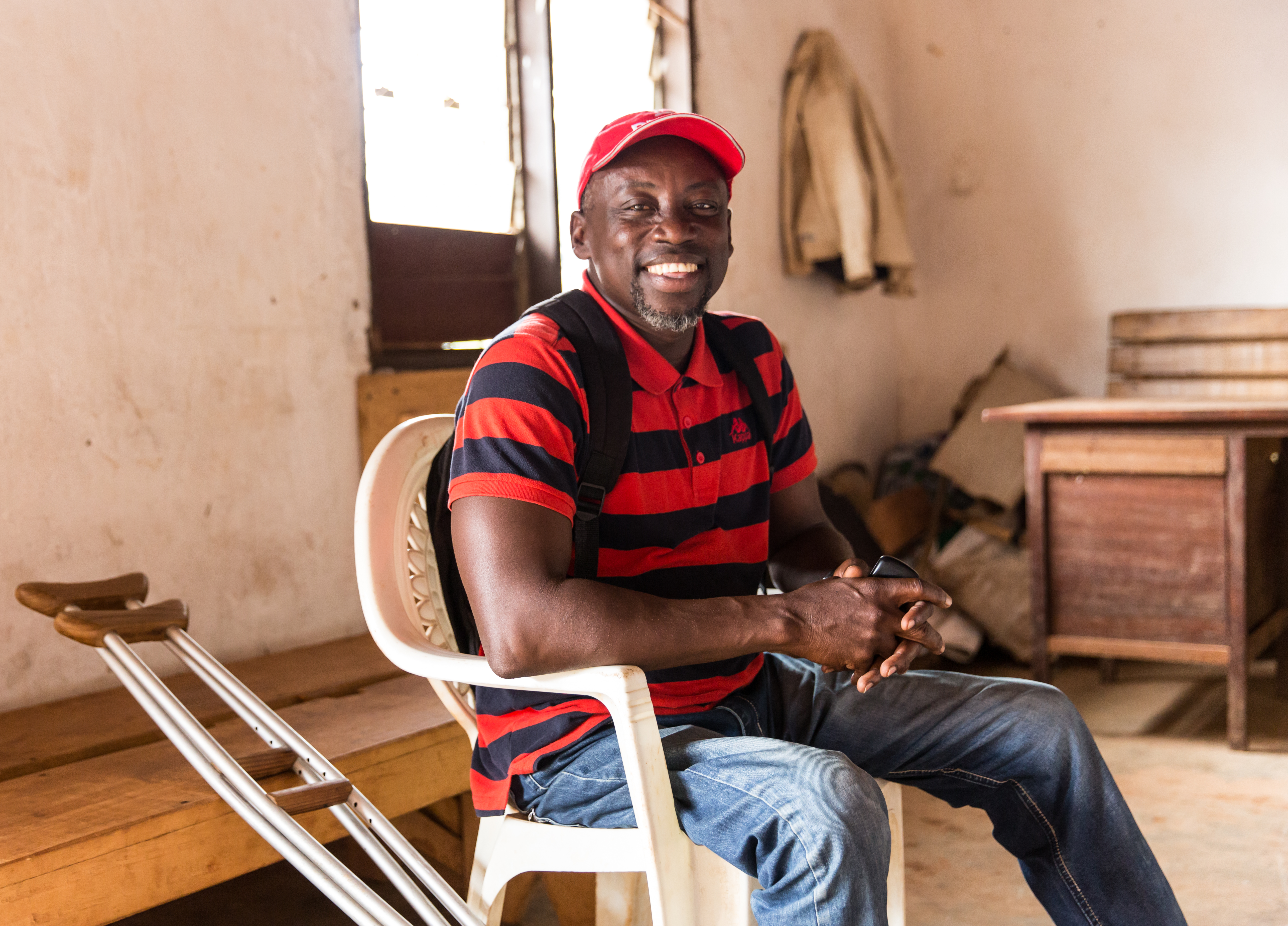 Image shows a man sitting in a chair, with crutches at his side