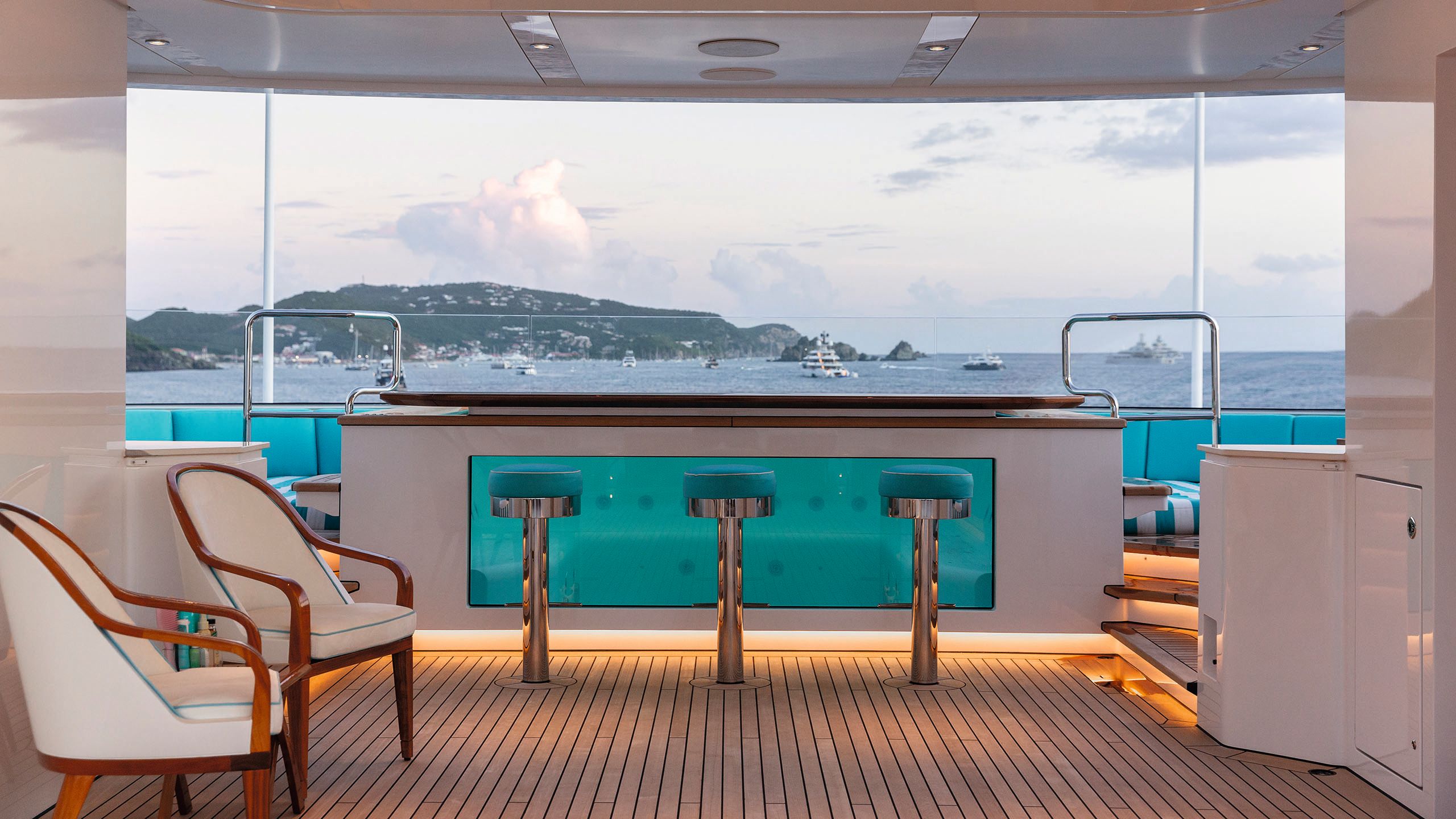 Looking at the pool from the side, from inside the deck looking out. There are stools and two chairs in the foreground