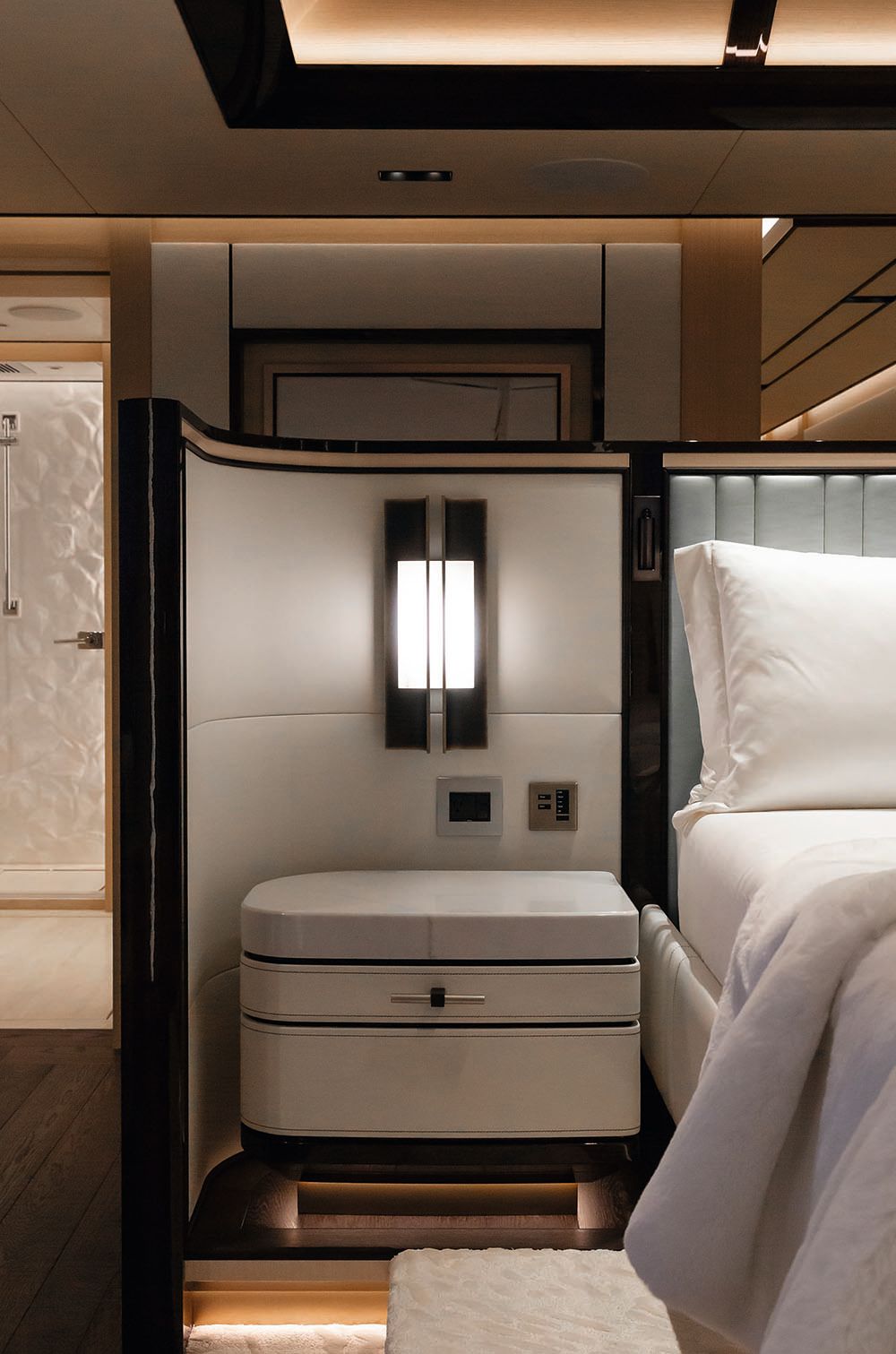 A bedside table next to a bed. The cabin is done in neutral colours and dark wood