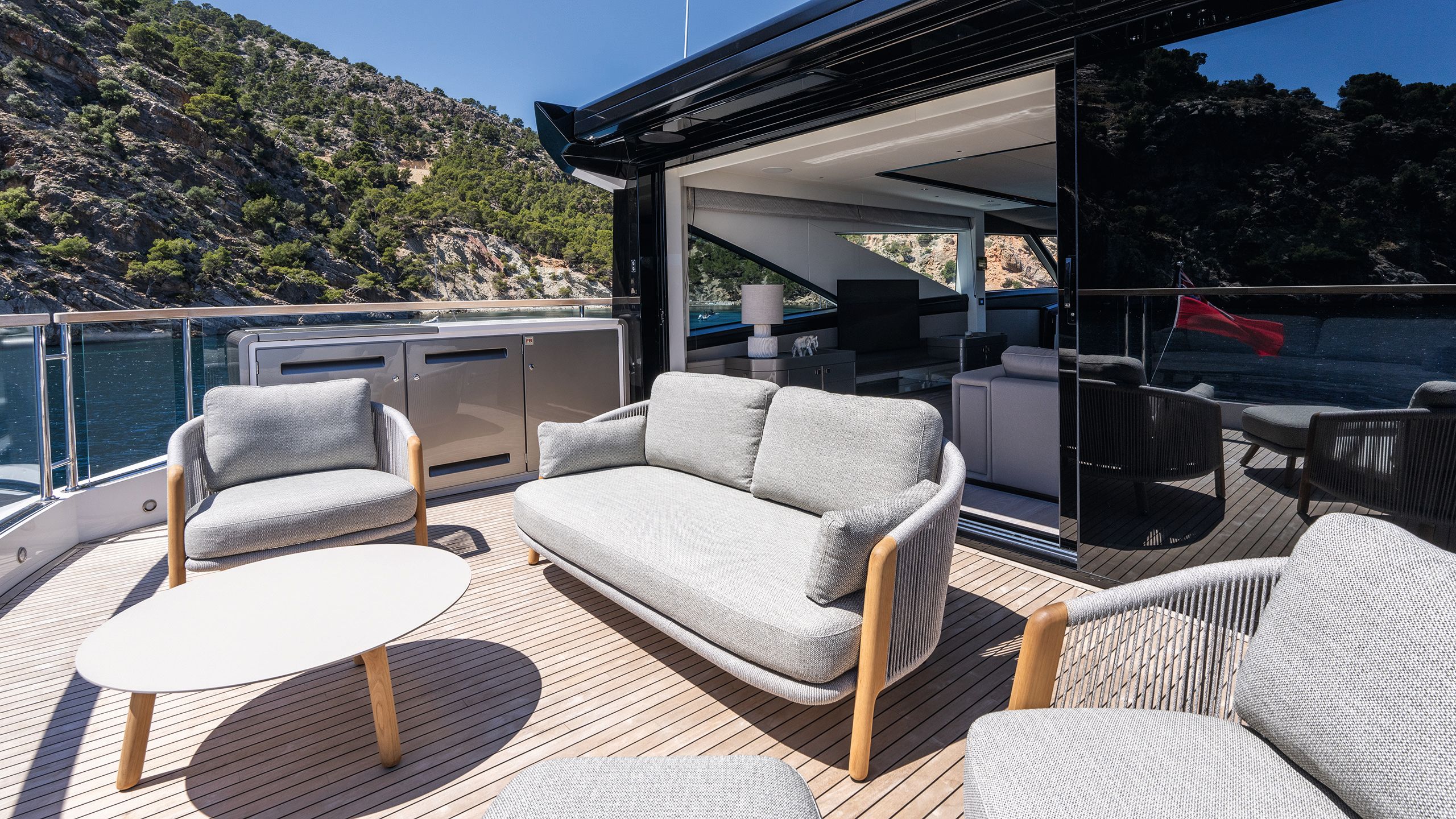 Outdoor sofa and chairs in grey and neutral wood with a white table, facing the sun on the deck