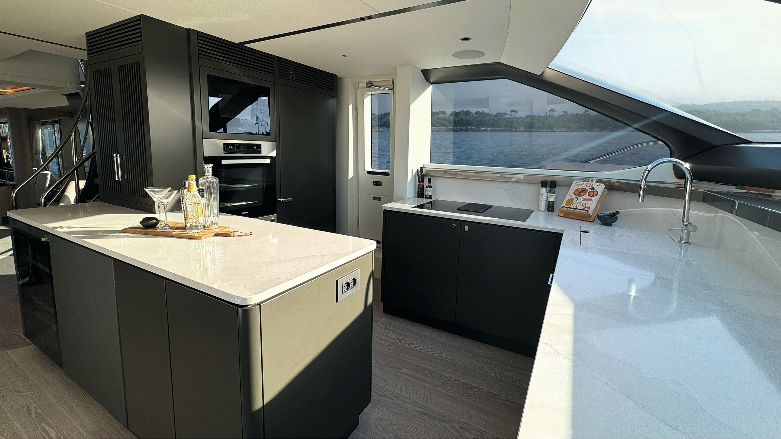 A close-up view of the marble counters, dark cabinets and sun streaming through the windows on to the fitted kitchen appliances
