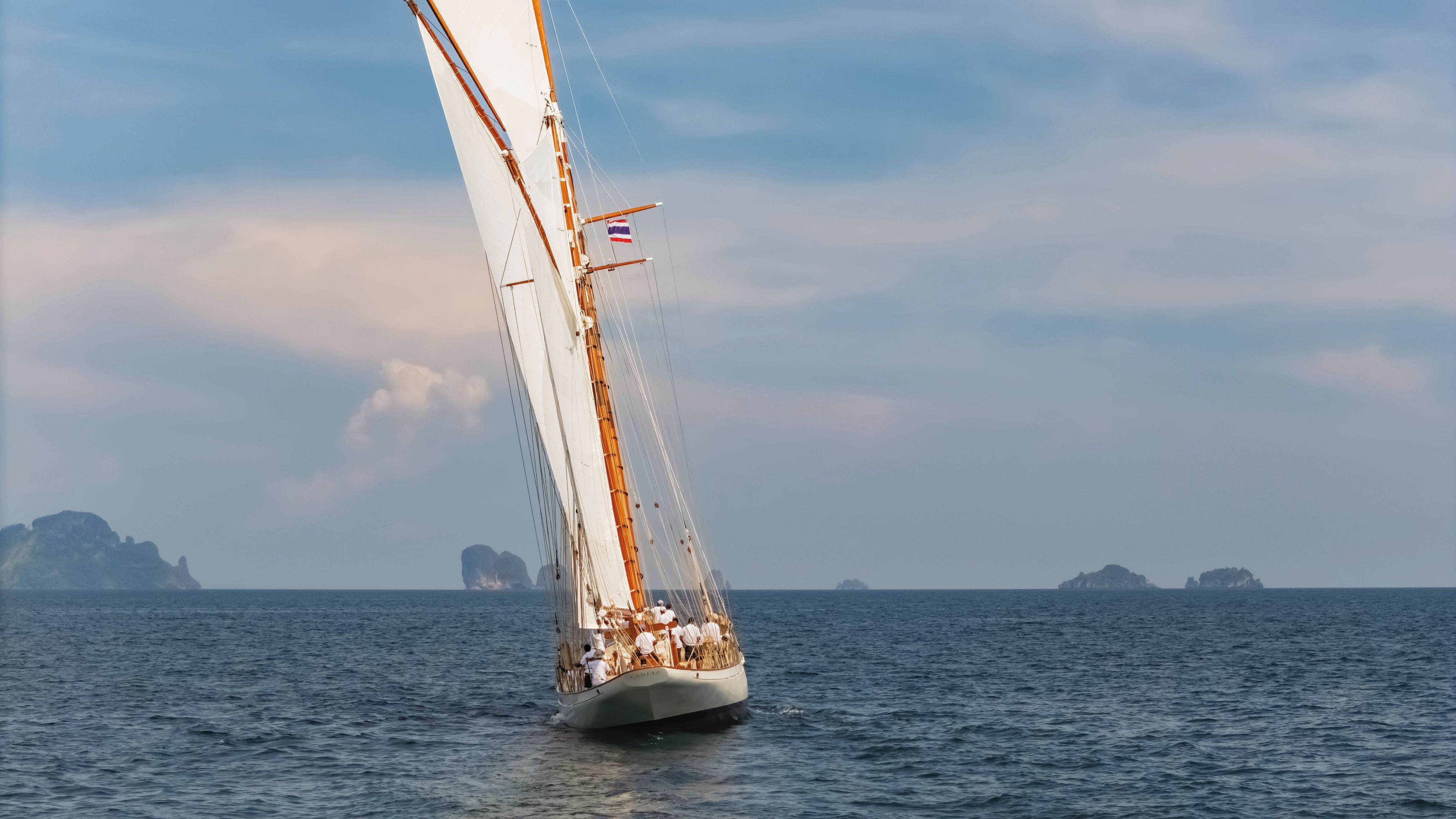 Cariad from the back with its sails out on the water - several people can be seen seated on the boat