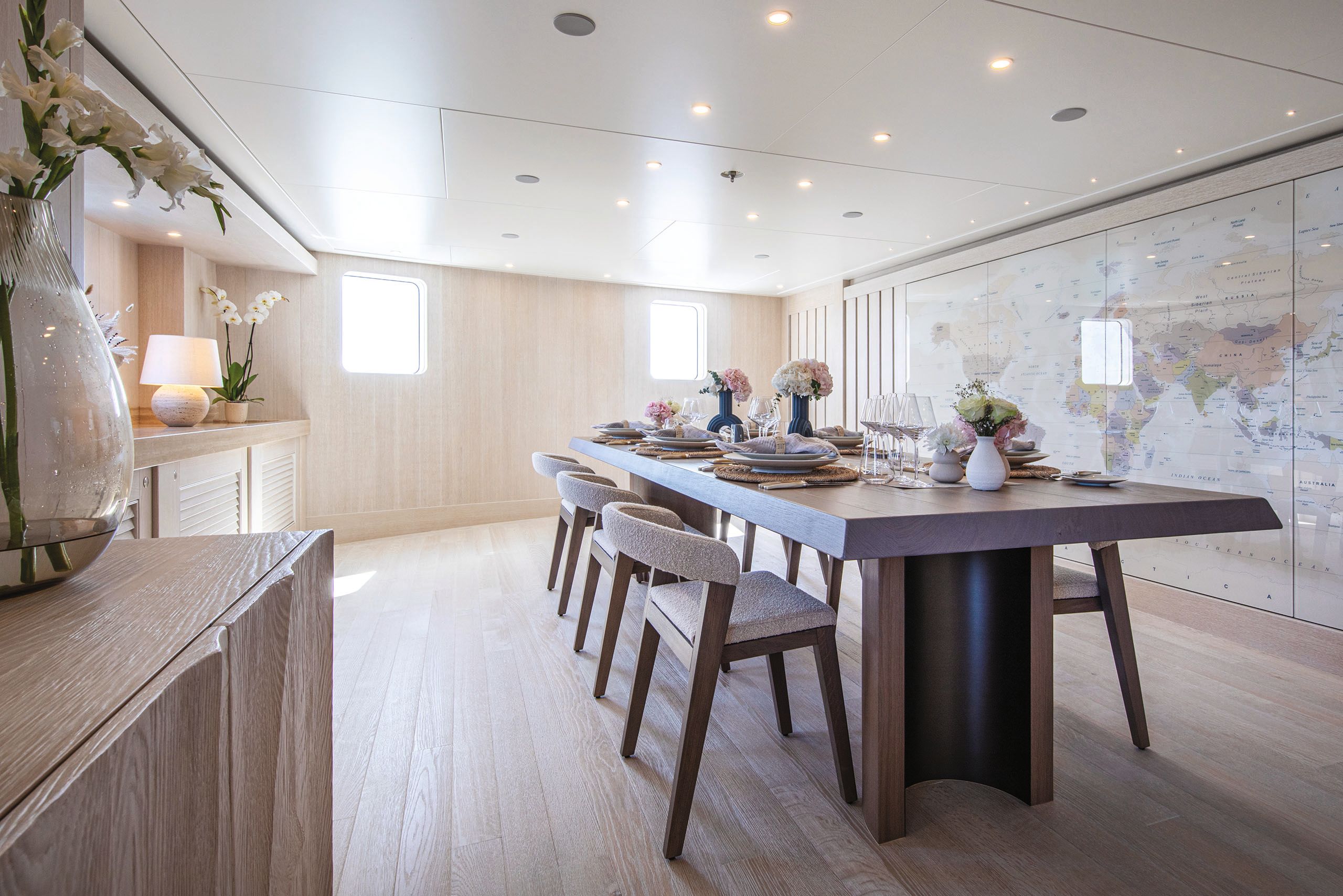 Bright room with long walnut colour table and chairs. There is a large map of the world on the wall