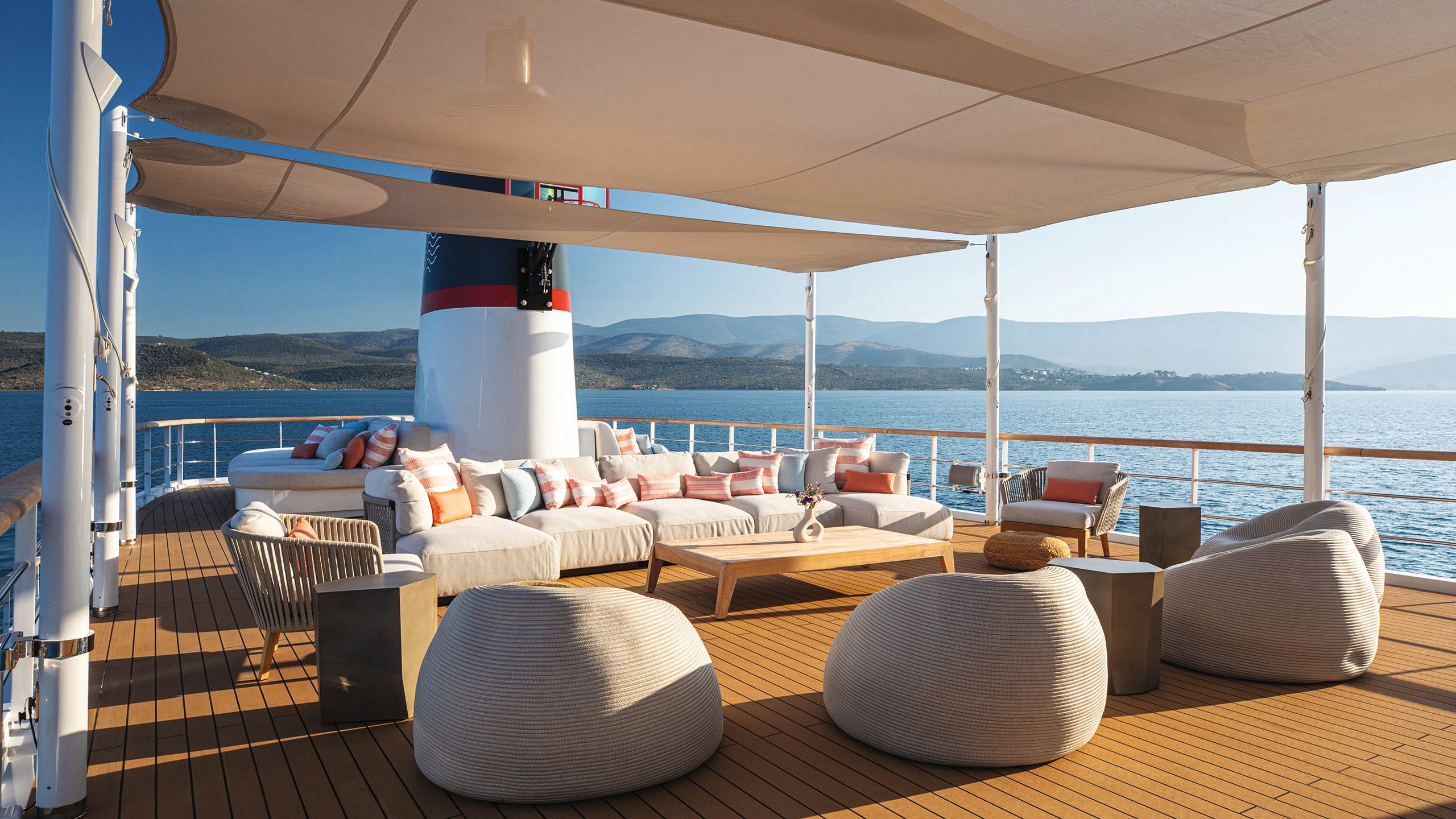 Soft-seating area on top deck which is also covered. There are large white sofas and wicker chairs with orange and white cushions