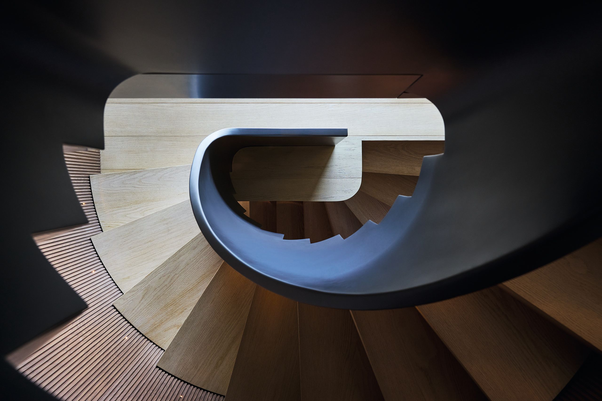 Looking down a spiral staircase with blue side, pale wood treads and ribbed panelling on the wall