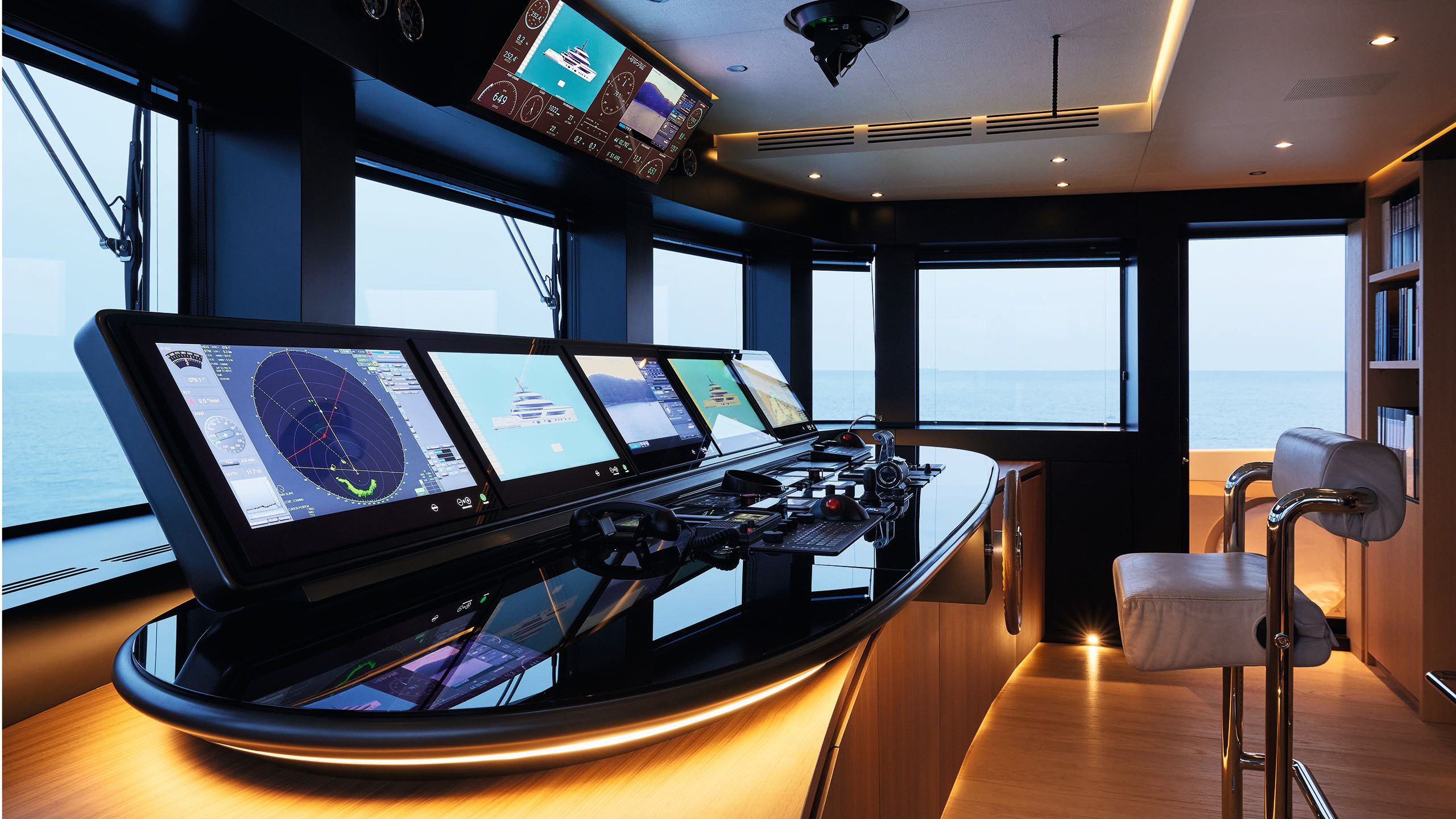 A bank of monitors facing a leather chair, looking out to the sea through large windows