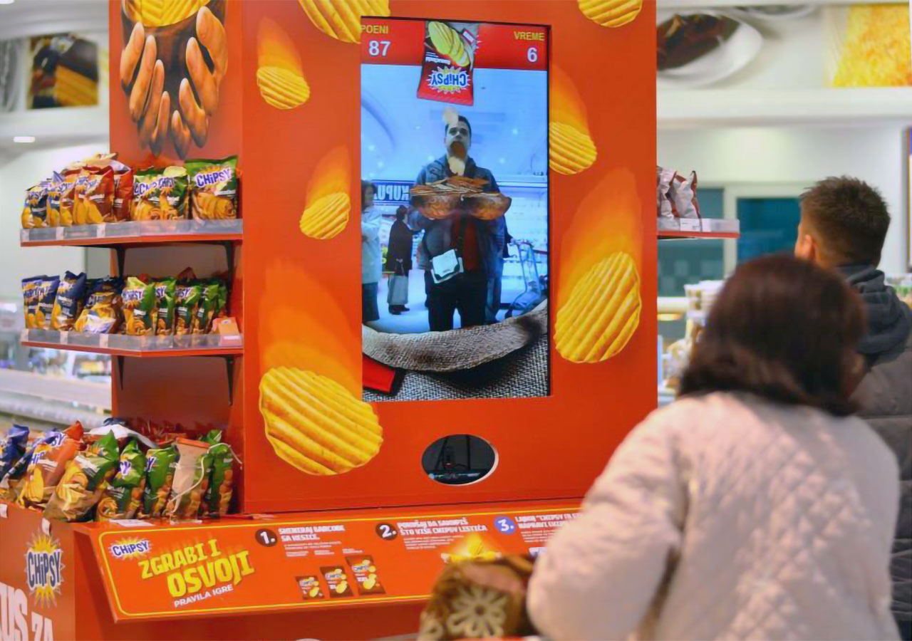 Supermarket customers engaging with an interactive Chipsy game kiosk, where players catch virtual chips using motion tracking technology.