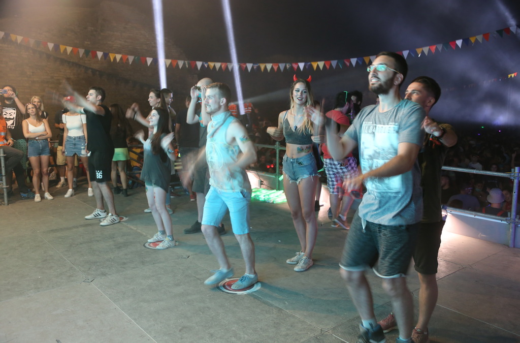 Audience members at an event engaging with a gaming activation, looking up at a large LED screen with vibrant graphics, some with raised arms, indicating interaction with the game.