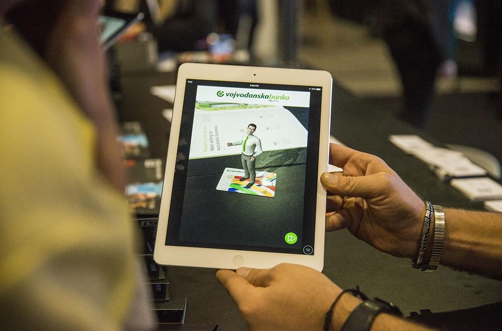 A person holds an iPad displaying Voban, Vojvođanska bank's virtual assistant, standing on a graphic of a bank card, showing off his ability to provide information interactively.