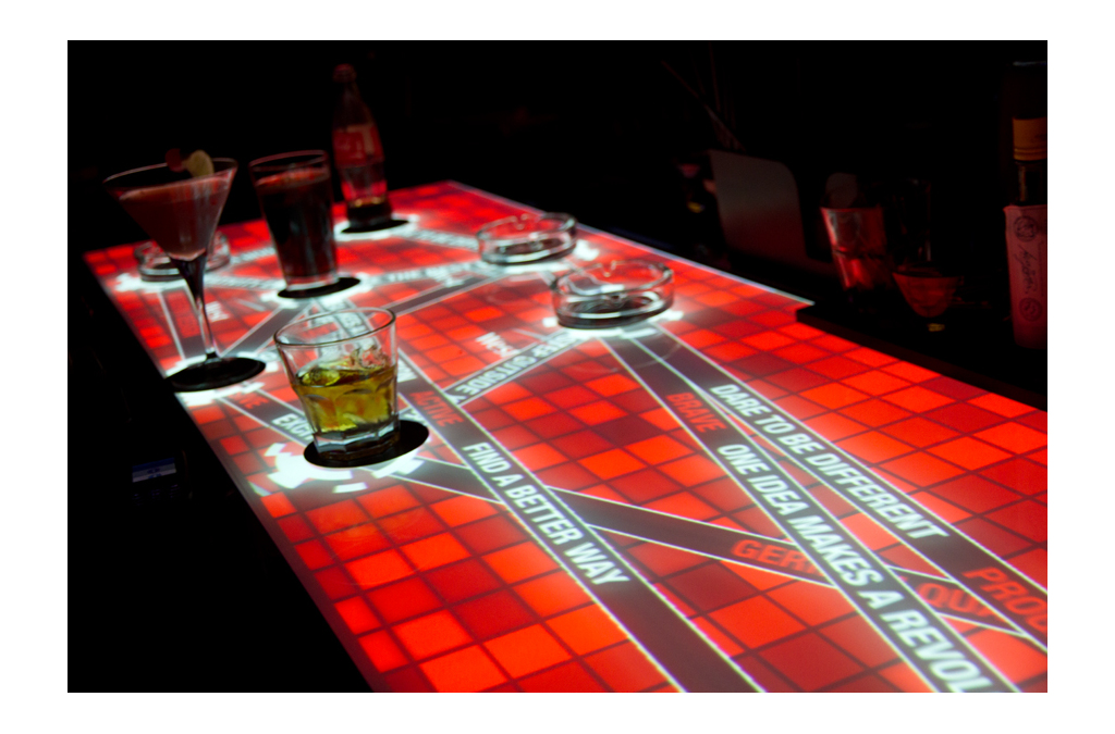 The bar counter showcases its interactive capabilities with a bright red digital interface, reacting to the placement of drinks and touch. 