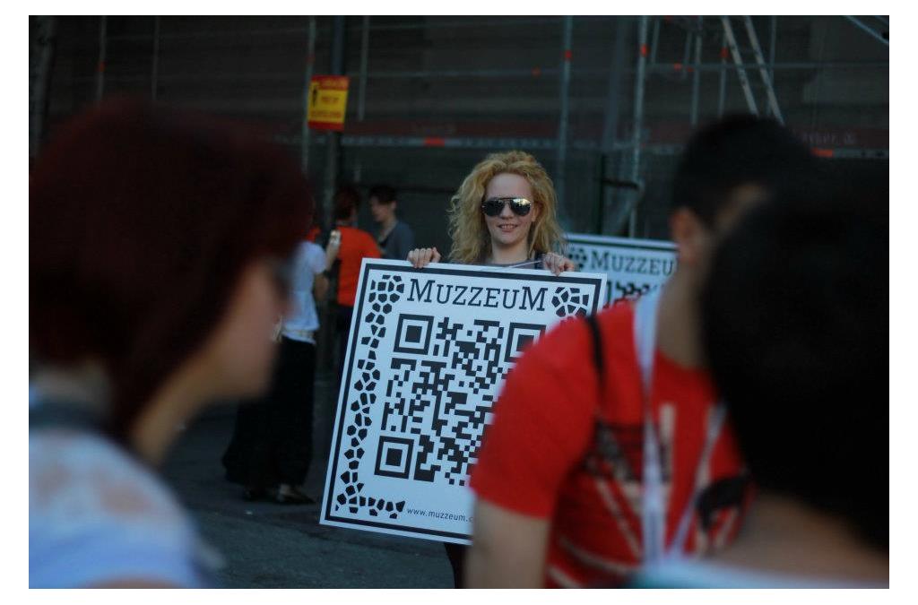 An individual holds up a MUZZEUM project ARQR code on a large sign, engaging the public with augmented reality to access virtual Serbian cultural heritage.