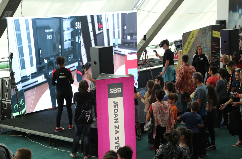 A lively scene at the Balkan TUBE Fest with attendees, mostly children, watching two players competing in an SBB VR game.