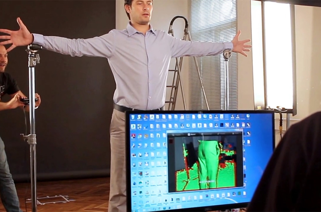  A behind-the-scenes view of a motion capture session for the Telenor Bank augmented reality app, with an actor wearing casual business attire standing with his arms extended. He is surrounded by motion-capture equipment, with a monitor in the foreground displaying the real-time capture of his movements.