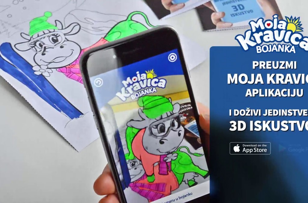 A child's coloring book page brought to life through the 'Moja Kravica' app on a smartphone, showing a cow character in 3D, demonstrating the app's augmented reality feature.