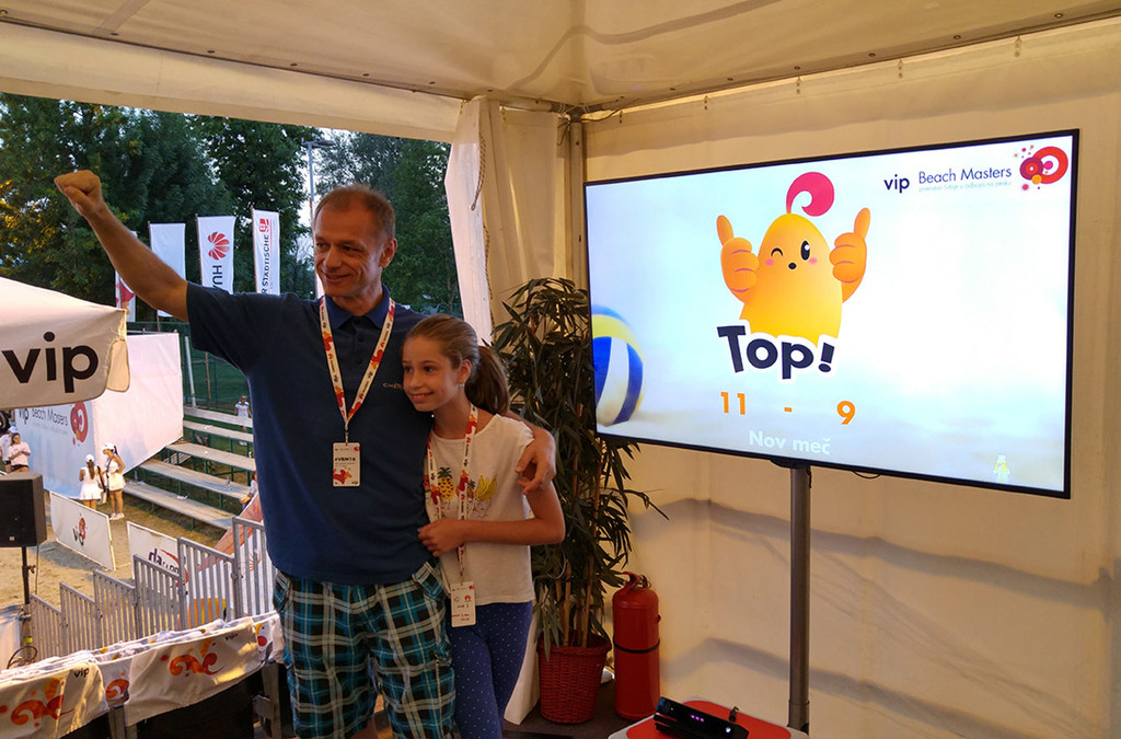 An adult and a child celebrate their score in a Kinect volleyball game at a beach volleyball event sponsored by VIP Mobile.
