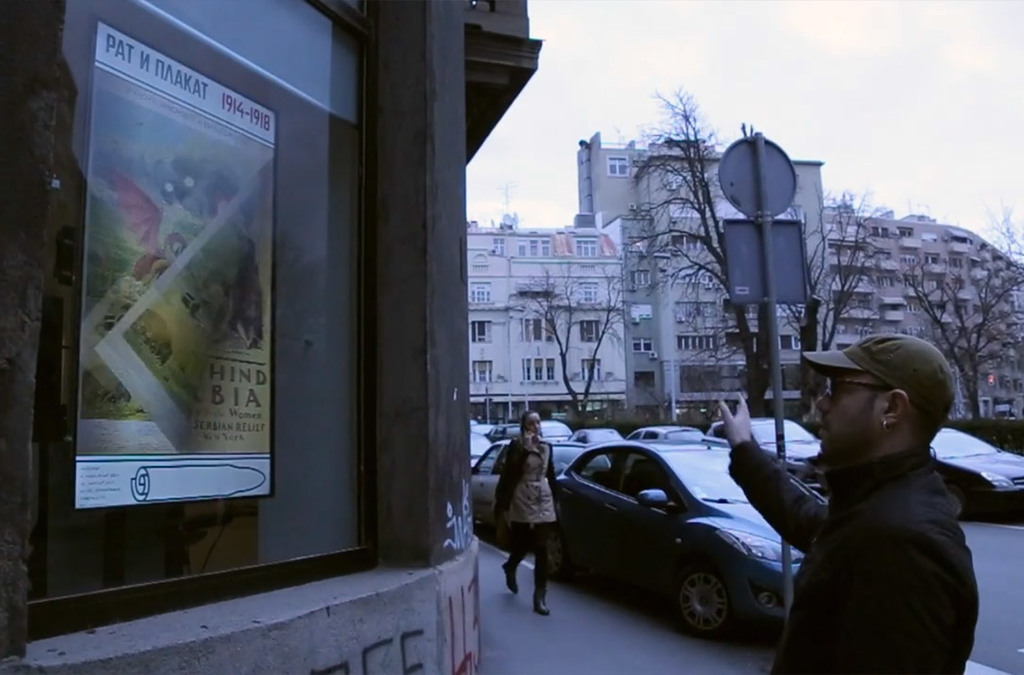 A person uses a light hand movement to interact with an outdoor interactive screen displaying a historical war poster.