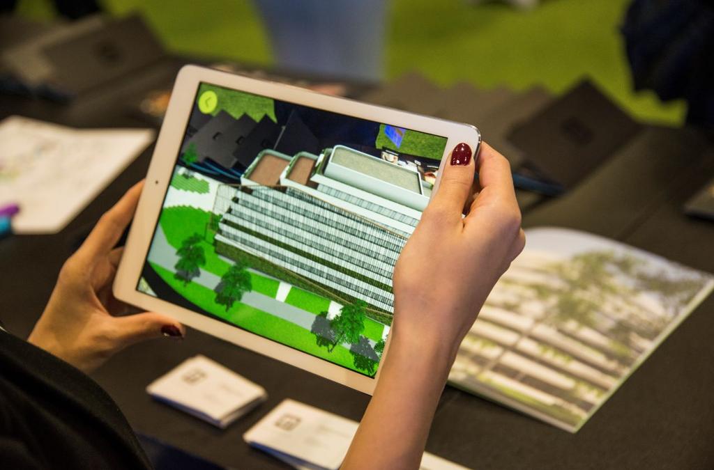 Close-up of a person holding an iPad displaying an augmented reality (AR) model of the GTC Green Heart Complex, overlaid on a physical brochure with the layout of the complex, demonstrating the innovative way of exploring real estate through AR technology.