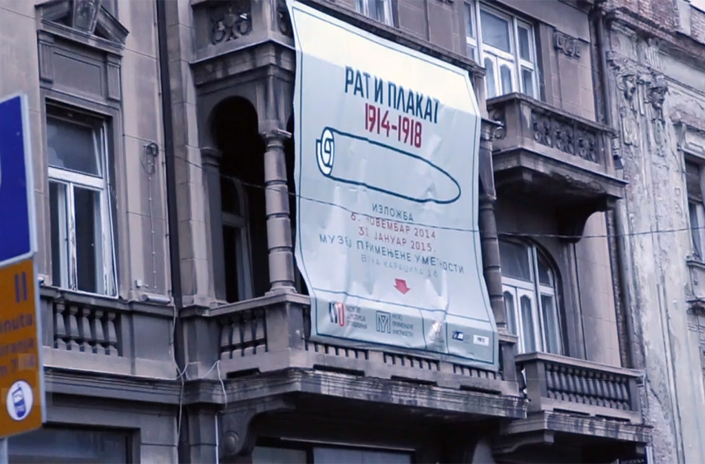A banner hanging on a building facade advertises the “Rat i Plakat” exhibition, extending the museum experience to the street.